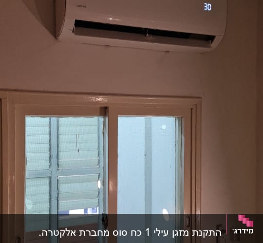 מזגן מותקן על קיר מעל חלון עם תצוגת טמפרטורה